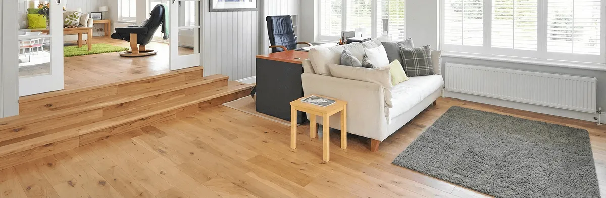 A modern living room with professionally installed laminate flooring, a beige sofa, a small side table, a gray rug, and large windows with white shutters in Indianapolis, IN